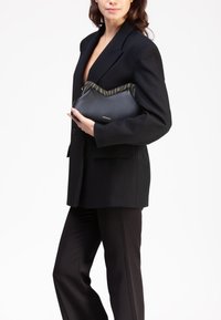Clutch in pelle nera con un bordo a zigzag verde e nero. Presenta un logo discreto. Forma curva con una texture liscia.