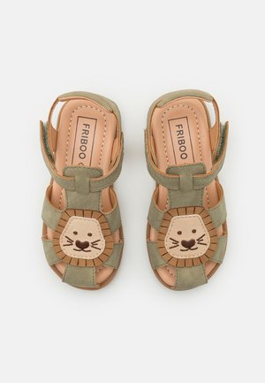 Grüne Kindersandalen mit Löwengesicht-Dekorationen auf den vorderen Riemen und verstellbaren Klettverschluss am Knöchel, innen mit "FRIBOO" beschriftet.