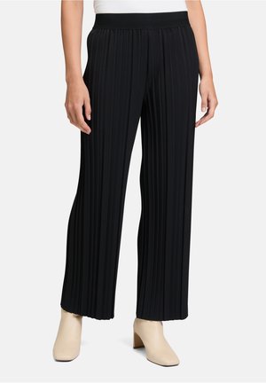 Pantaloni neri a pieghe con gamba larga realizzati in un tessuto strutturato, con una vita elastica, abbinati a scarpe beige con tacco a blocco.