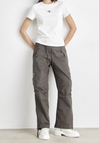 Bílá těsně padnoucí tričko s malým logem, spárované s volnými šedými cargo kalhotami s kapsami a stahovací šňůrkou, doplněné chunky bílými botami.