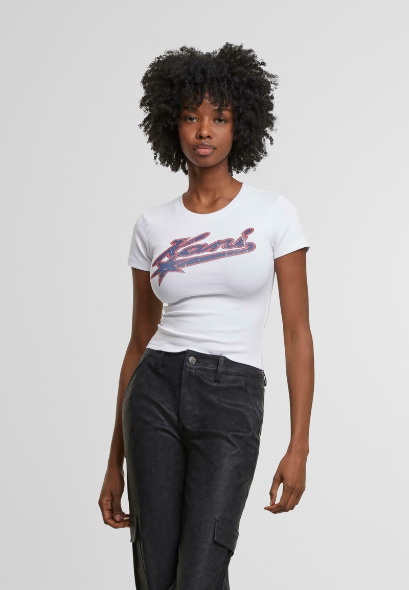 Camiseta ajustada blanca con un diseño gráfico de texto en rojo y azul, combinada con pantalones negros de talle alto que cuentan con bolsillos laterales y una tela texturizada.