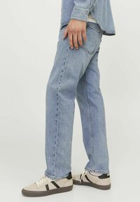 Svijetloplavi traperice ravnog kroja, s blagim izbljeđivanjem i šivenim detaljima. Uparene s bež tenisicama i crnim naglascima.