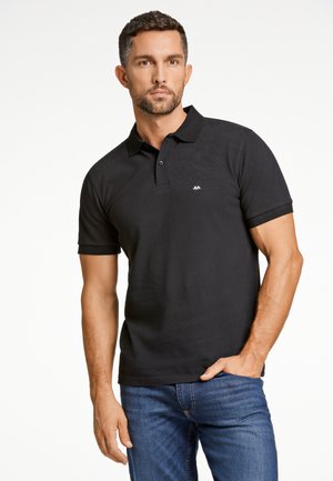 Camisa polo negra de tejido texturizado, con una tapeta de dos botones y un pequeño logo en el lado izquierdo del pecho. Combinada con jeans azules.