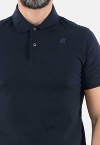 Polo shirt blu nave in cotone, presenta una patta con bottoni, colletto a coste e un logo discreto sul petto. Maniche corte, texture liscia.