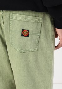 Light green denim pants with a back pocket featuring a black "Santa Cruz" logo patch. Smooth texture and casual fit design.