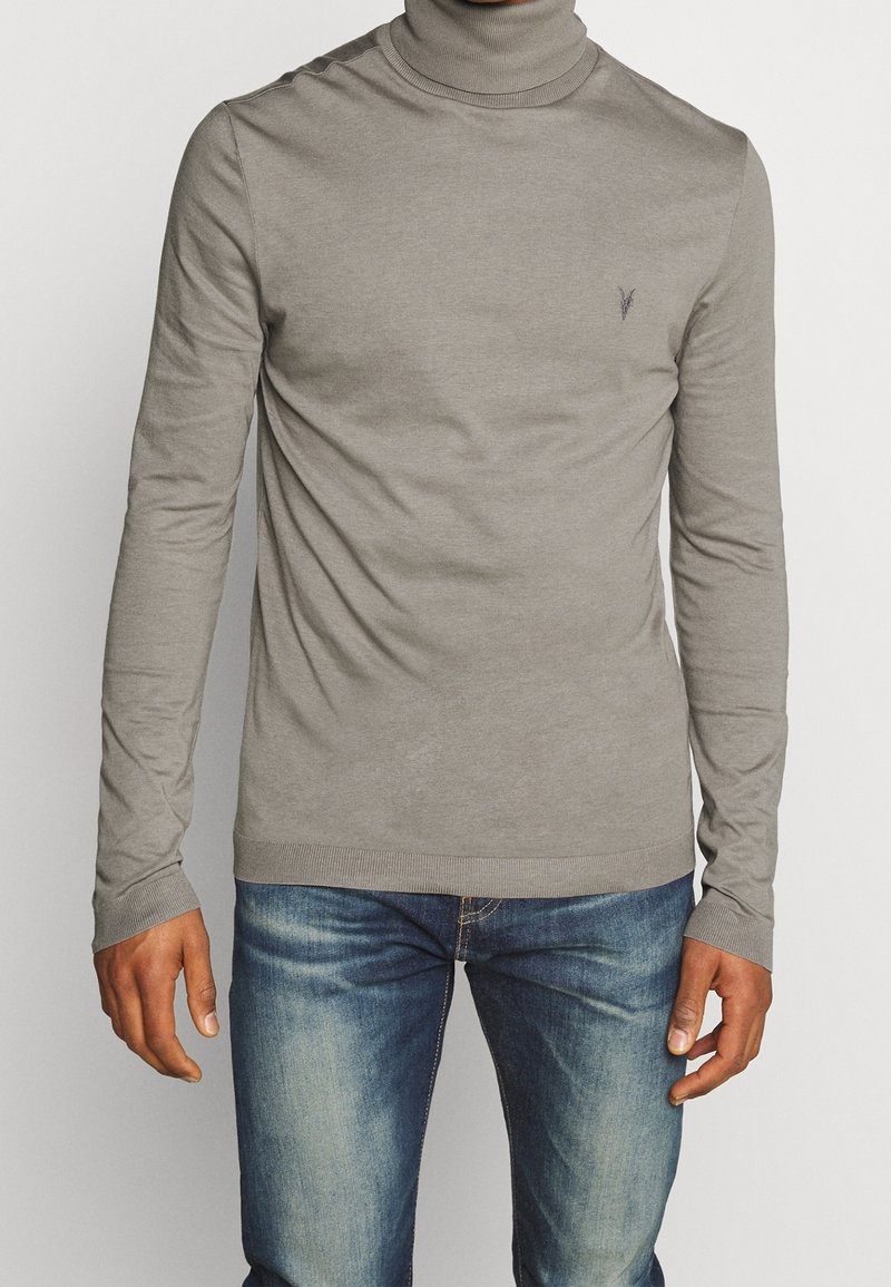 Grå polotröja i mjukt tyg, har lång ärmar, ribbade muddar och en liten logotypdetalj på bröstet. Matchas med blå jeans.