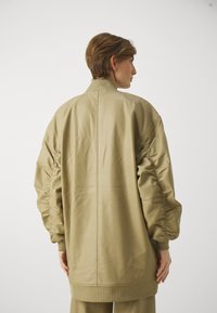 Preširoká khaki bomber bunda z hladkého, lesklého materiálu s rebrovanými manžetami a golierom. Má na rukávoch zberové detaily.
