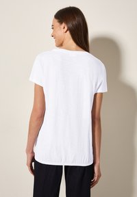 Witte T-shirt met korte mouwen, relaxed fit, ronde halslijn en een iets langere achterkant. Gestructureerde stof met een lichtgewicht uitstraling.
