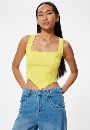 Gul croppad topp med fyrkantig halsringning, texturerad tyg och scallopkant, kombinerad med ljusblå högmidjade jeans med lätt slitage.
