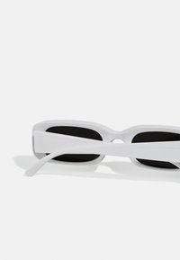 Lunettes de soleil blanches avec une forme rectangulaire, finition brillante et verres noirs. Branches larges avec un design courbé pour le confort.