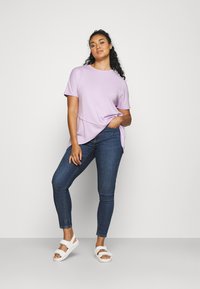 Light purple short-sleeve top paired with dark skinny jeans and white strap sandals. The top features a curved hem and relaxed fit.