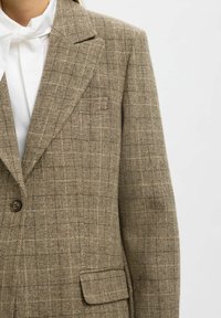 Blazer marron à carreaux avec un tissu texturé, des revers crantés, une fermeture à un bouton et une poche à l'avant.