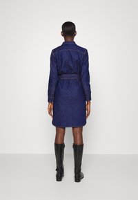 Denim skjortklänning i mörkblått, med bälte i midjan, knäppningsärmar och raka fållar. Bärs med svarta stövlar upp till knäna.