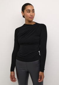 Schwarzes Langarmoberteil mit drapiertem Design. Hergestellt aus dehnbarem Material, mit Rundhalsausschnitt und schmaler Passform, kombiniert mit grauen Leggings.