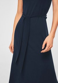 Navy blue dress featuring a fitted bodice, wide waistband, and long tie detail. Made of smooth fabric with a slightly textured finish.