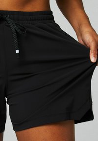 Schwarze Sportshorts aus glattem, elastischem Stoff mit einem elastischen Bund und Kordelzug; verfügen über seitliche Schlitze für mehr Flexibilität.