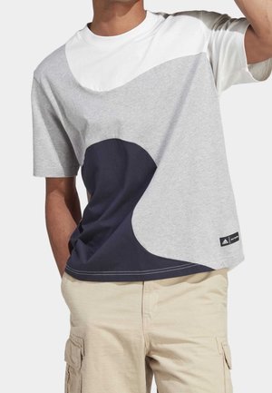 Homme portant un t-shirt à manches courtes à blocs de couleurs blanc, gris et bleu marine, ainsi qu’un short cargo beige avec poches.
