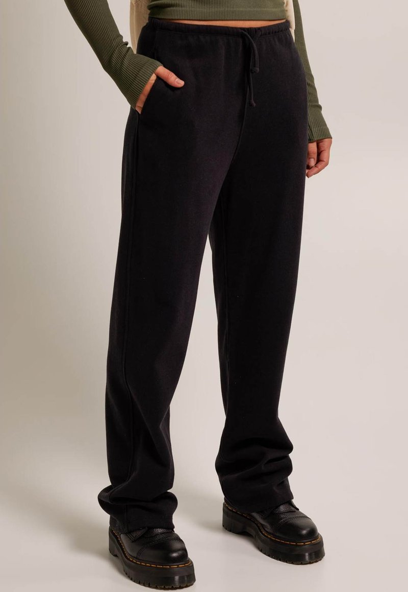 Black jersey sweatpants with an elastic waistband, drawstring detail, and side pockets, paired with black lace-up boots.