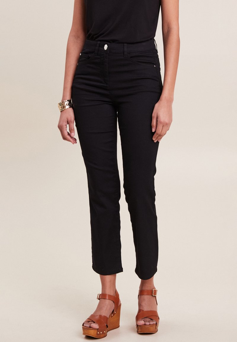 Jean noir à jambe droite avec une taille haute, comportant des poches avant, une fermeture éclair et une texture lisse. Porté avec des sandales à plateforme marron.