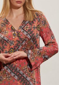 Vestido de manga larga y escote en V en coral y oliva, con patrones florales y geom�étricos, detalles en negro y un diseño fluido.