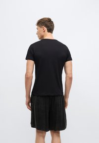 Μαύρο κοντομάνικο t-shirt από μαλακό βαμβάκι. Απλό σχέδιο με στρογγυλή λαιμόκοψη, εφαρμοστή γραμμή και ελαφρώς μακρύτερο πίσω μέρος.