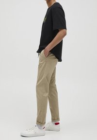 Svart bomullströja med grön grafik, tillsammans med beige bomullsbyxor. Vita sneakers med röda och blå detaljer, avslappnad passform.