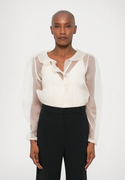 Blouse blanche transparente avec un col volanté et de longues manches transparentes, associée à un pantalon noir sur mesure. Texture lisse et design élégant.