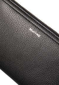 Cartera de cuero negra con una superficie texturizada y un zipper dorado. Presenta el logo en relieve "MAITRE" en blanco cerca de la parte superior.