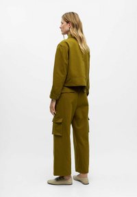 Veste en coton vert olive avec épaules tombantes et pantalon cargo assorti, doté de poches latérales et d'une coupe décontractée. Chaussures plates simples.