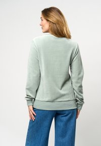 Ljusgrön sweatshirts med rund halsringning, långa ärmar och ribbade muddar. Tillsammans med vida blå denimbyxor.