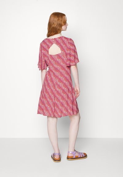 Vestido com padrão vermelho, com mangas curtas e soltas e detalhe de abertura nas costas, combinado com sandálias lavanda e solas castanhas.