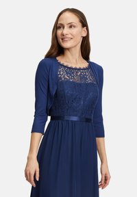 Robe bleu marine avec un corsage en dentelle, manches trois-quarts et accent en satin. La texture fluide de la jupe ajoute élégance et mouvement.