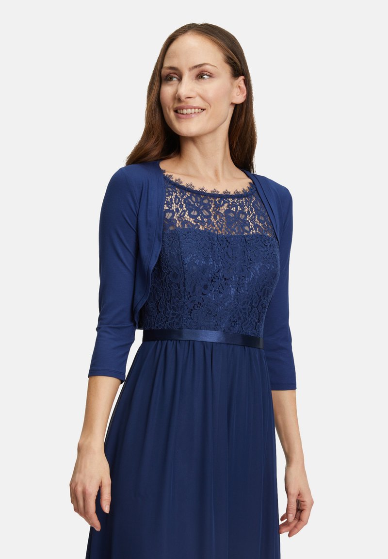 Robe bleu marine avec un corsage en dentelle, manches trois-quarts et accent en satin. La texture fluide de la jupe ajoute élégance et mouvement.