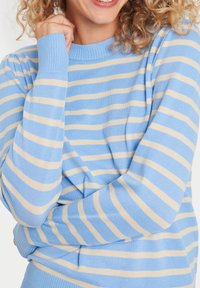 Pull bleu clair avec des rayures crème, encolure et poignets côtelés, texture douce, présentant une coupe décontractée et des manches légèrement froncées.