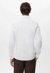 Biała koszula z długim rękawem wykonana z gładkiej tkaniny. Posiada klasyczny kołnierz i mankiety na guziki. Widok z tyłu pokazuje lekko zaokrąglony dół.