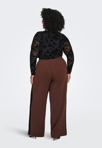 Black long-sleeve top with floral lace detail paired with brown wide-leg pants featuring black side panels and a relaxed waistband.