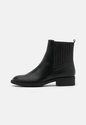 Bottine noire en cuir avec panneau latéral côtelé élastique, petit talon bloc et languette à l'arrière sur fond blanc.