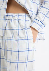 Ensemble de vêtements d'intérieur en coton à carreaux bleu et blanc, comprenant une chemise ample et un pantalon avec taille élastique et poches latérales.