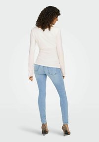Lys cremefarvet langærmet top parret med lyseblå skinny jeans. Outfittet har en tætsiddende pasform og bløde stofteksturer. Brune højhælede sko.