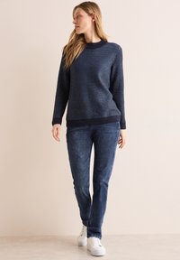 Golf di lana blu navy con un motivo testurizzato, collo rotondo e polsini a coste, abbinato a jeans slim di colore blu scuro e sneakers bianche.