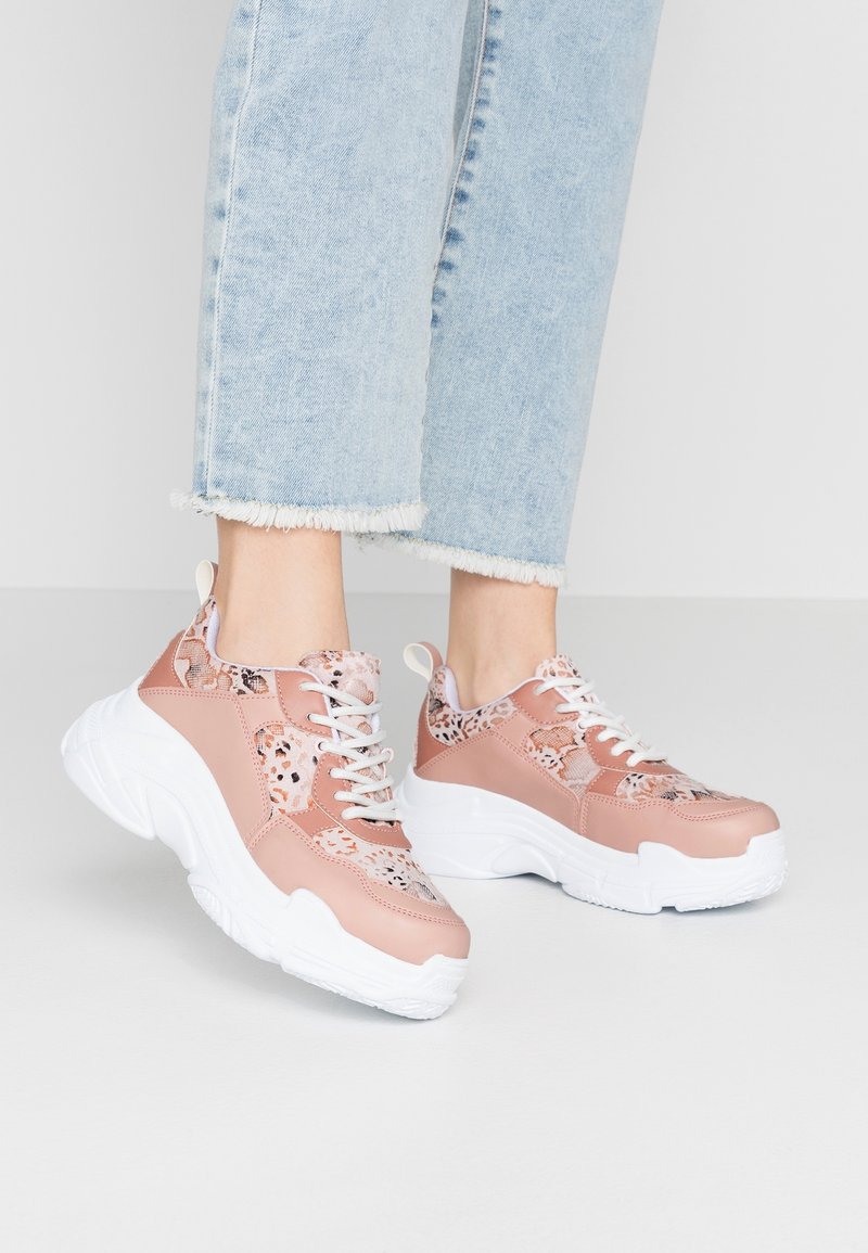 Jean court bleu clair porté avec des baskets épaisses roses et blanches affichant un motif floral et des semelles blanches épaisses.
