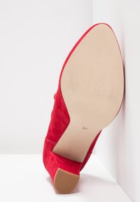 Chaussure à talon haut en suede rouge avec une semelle beige lisse, présentant une légère inclinaison à l'arrière et un design à bout carré. Taille 37 indiquée sur la semelle.