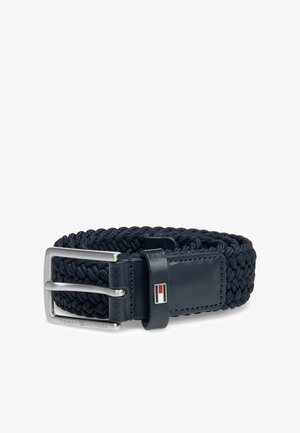 Ceinture en tissu tressé bleu marine avec accents en cuir, boucle métallique argentée et petit détail du logo Tommy Hilfiger rouge, blanc et bleu.