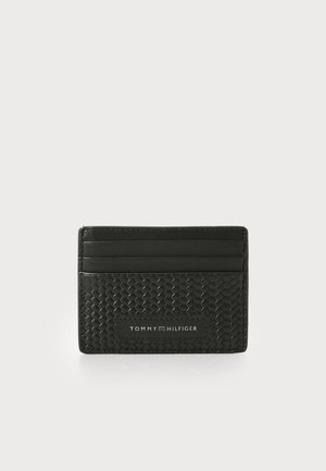 Black cardholder made from textured woven material with smooth leather accents. Features four card slots and a logo patch on the front.