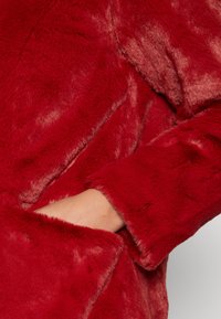 Rød imiteret pelsjakke med en blød, plysset tekstur. Lange ærmer med en afslappet pasform og sidelommer for ekstra bekvemmelighed.