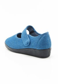 Zapato de tela azul con una correa de Velcro y una suela de goma negra texturizada. Parte trasera redondeada y cortes laterales para transpirabilidad.