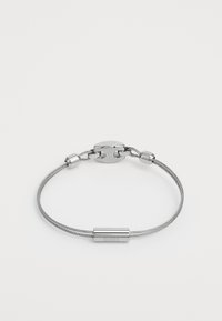 Sølvtrådarmbånd med en glatt metallklips og sylindriske aksenter. Designet er minimalistisk med en strømlinjeformet tekstur.