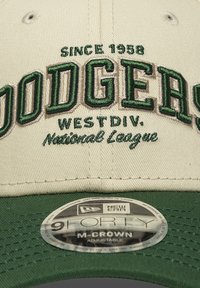 Μπεζ μπέιζμπολ καπέλο με πράσινη κεντητική. Περιλαμβάνει τα κείμενα «DODGERS», «SINCE 1958», «WEST DIV.» και «National League». Ρυθμιζόμενο λουράκι.