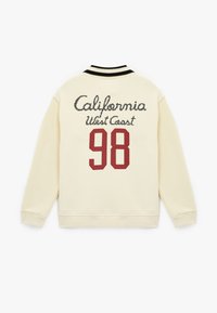 Kremowa bluza z czarnymi akcentami, z napisem "California West Coast" oraz numerem "98" w burgundowym kolorze na plecach.