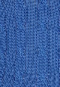 Blå stickad tyg med ett texturerat kabelmönster med upphöjda öglor, vilket skapar ett visuellt distinkt och strukturerat utseende.